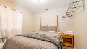 Un dormitorio con cama, mesita de noche de madera, toallero y cortina de ducha.