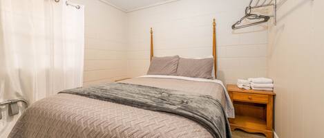 A bedroom with a bed, a wooden nightstand, a towel rack, and a shower curtain.