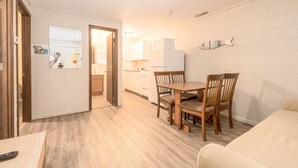 Una cocina compacta con armarios blancos, una mesa de comedor de madera con cuatro sillas y un refrigerador blanco.