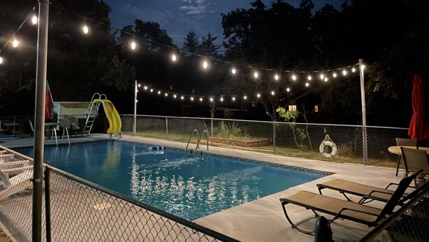 A swimming pool with a slide, surrounded by a fence, and string lights overhead. - Resort 2bdrm condo on Table Rock Lake, by SDC! (Branson)