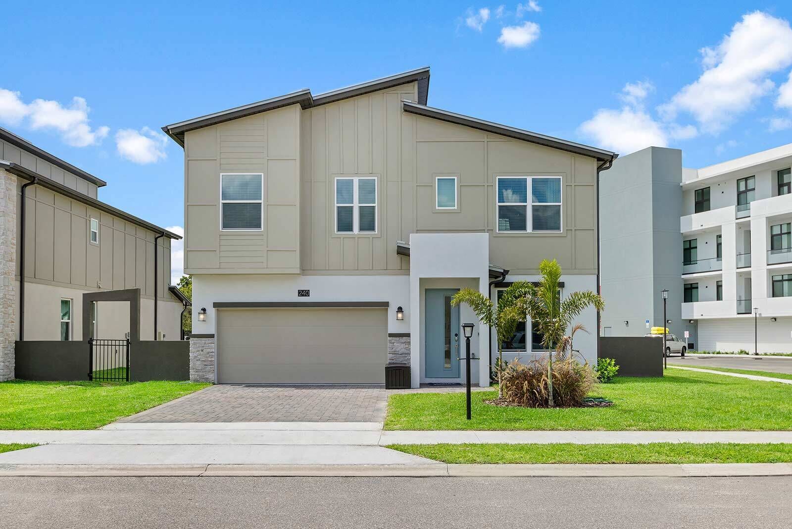 A modern two-story residential building with a garage, a well-maintained lawn, and a clear sky.