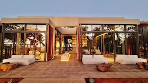 A modern house with large glass windows, a wooden deck, and outdoor seating. - Hamares Boutique Hotel (Fernando de Noronha)