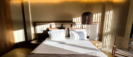 Una habitación de hotel con una cama grande, una mesita de noche con lámpara y una silla.