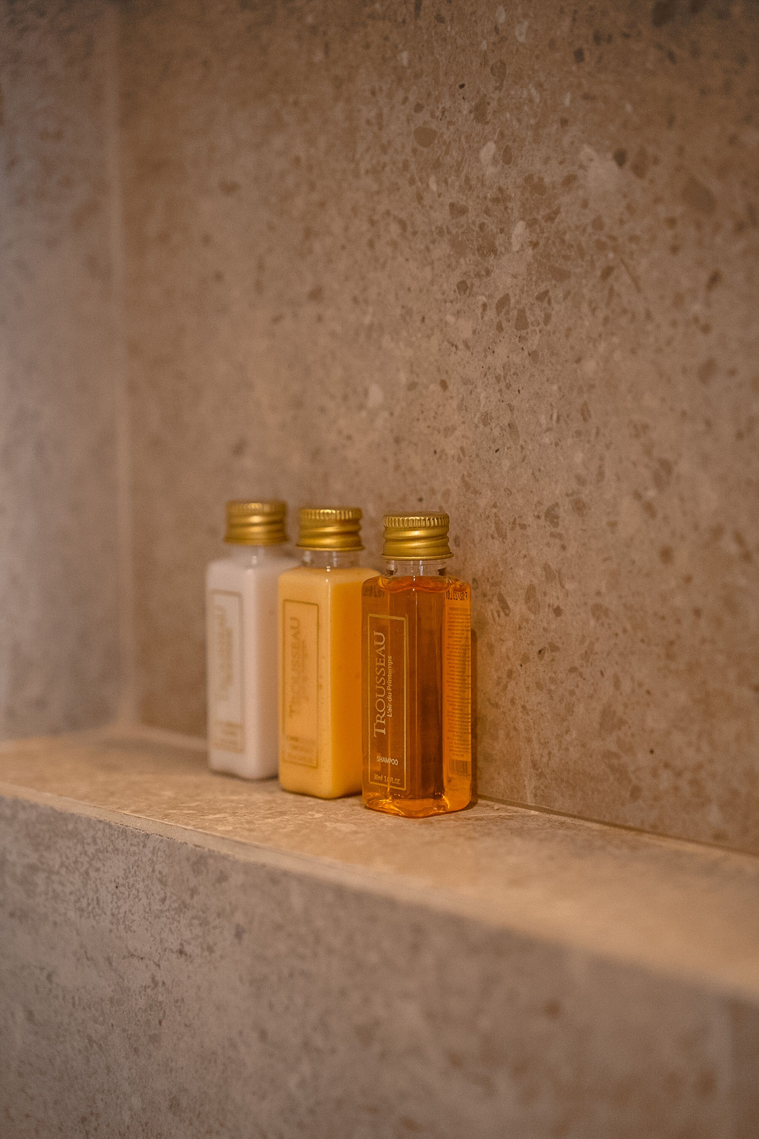 Three bottles of liquid on a shelf against a textured wall.