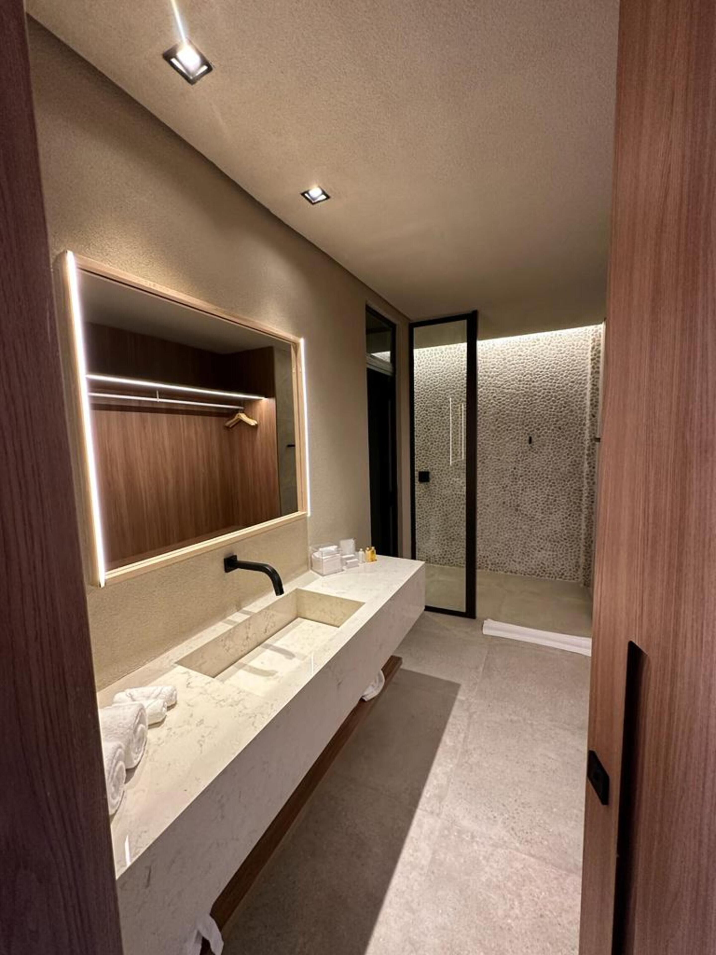 Un baño moderno con un espejo grande, lavamanos dobles y ducha a ras de suelo.