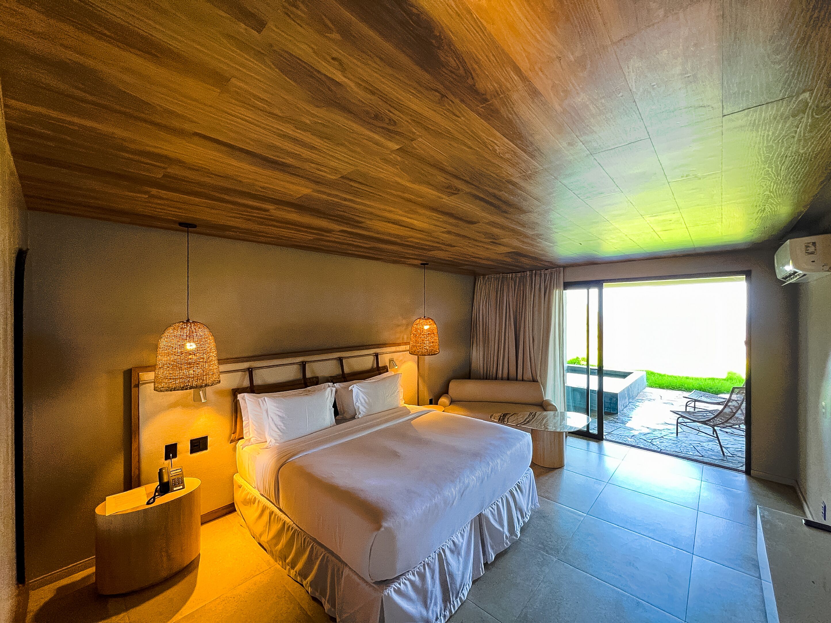 A bedroom with a large bed, bedside lamps, a telephone, and a view of the outdoors.