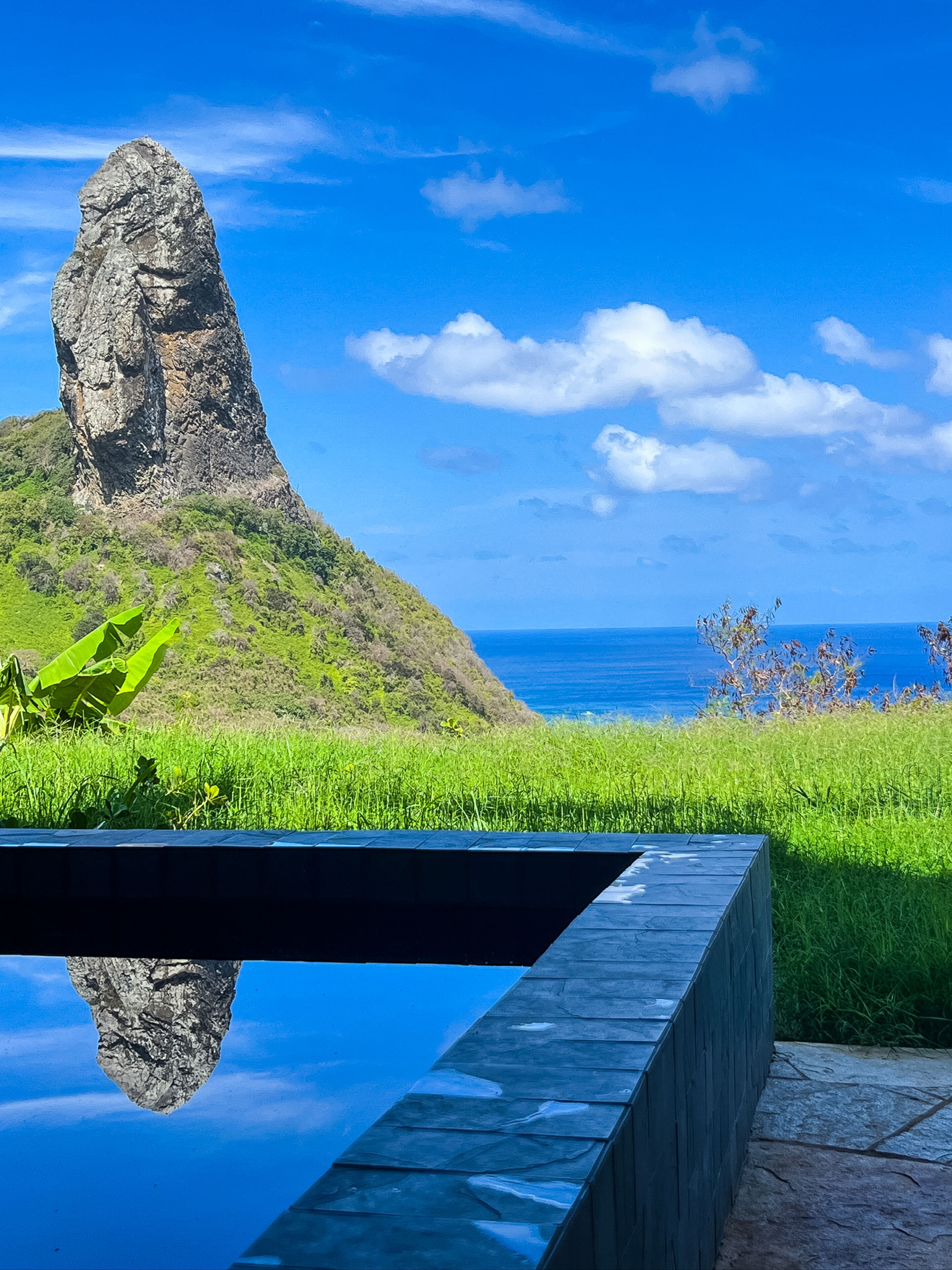 A pool with a clear view of a rocky hill and ocean.