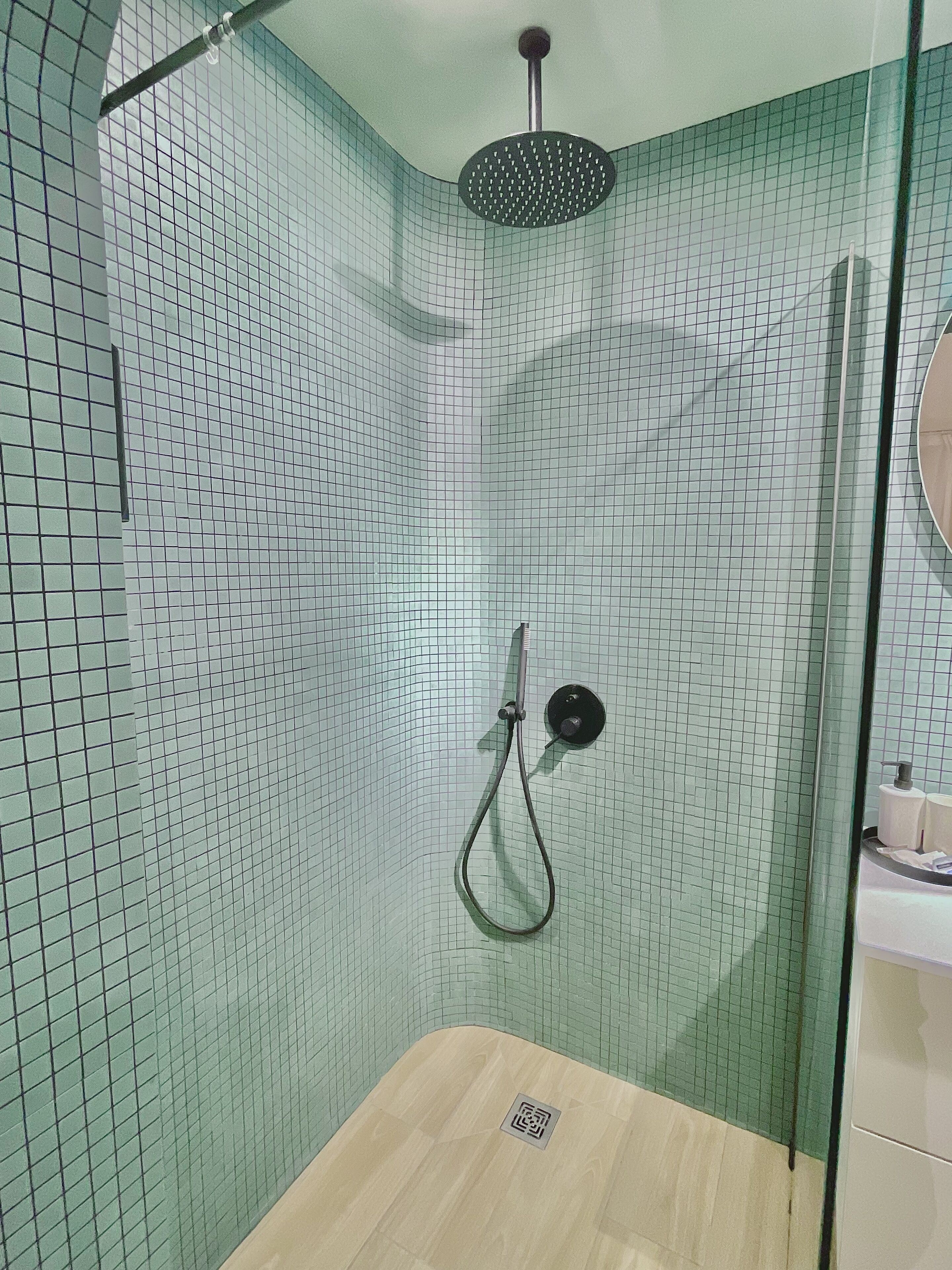 Une douche équipée d’un pommeau de douche à main, d’une porte en verre et d’un mur carrelé.