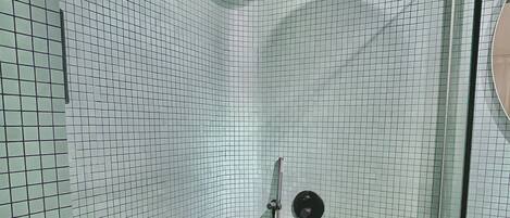 Une douche équipée d’un pommeau de douche à main, d’une porte en verre et d’un mur carrelé.