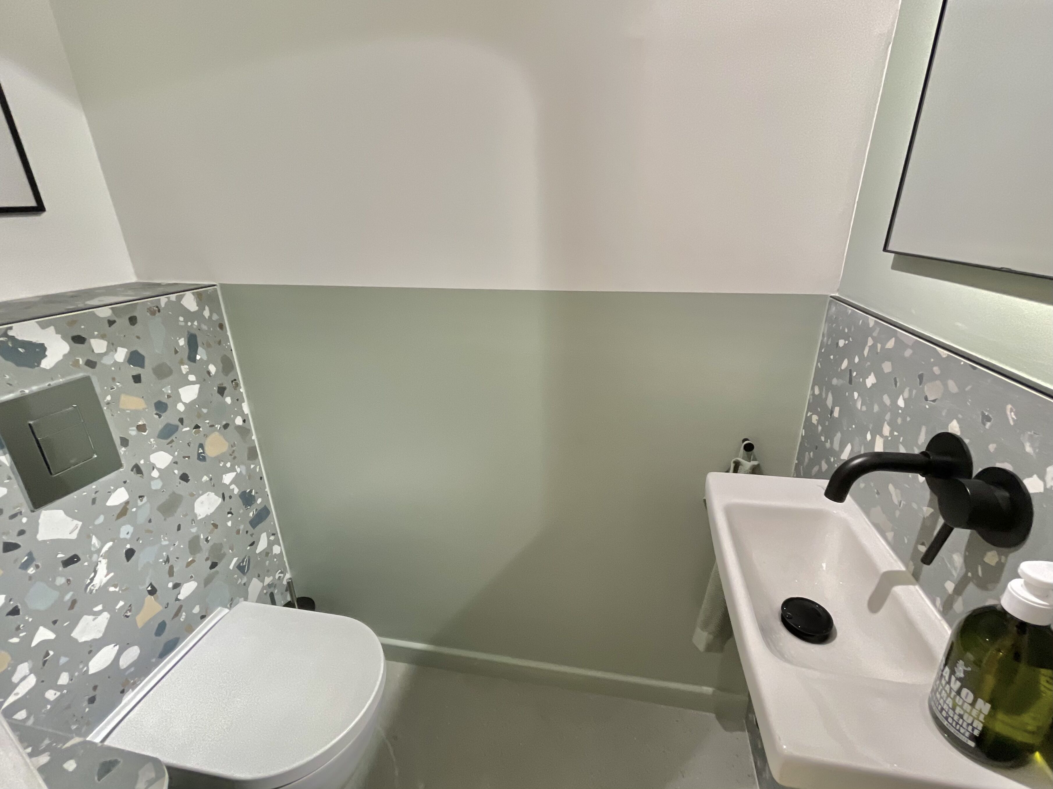 A bathroom with a white toilet, a sink with a black faucet, and a mirror above the sink. The walls have a terrazzo tile design.