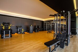 Een moderne sportschool met diverse fitnessapparaten, houten vloeren en een bankje.