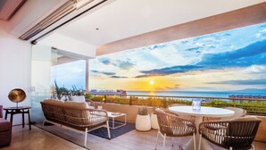 Un espace extérieur moderne, aménagé avec des meubles en osier, une table ronde et offrant une vue sur le coucher de soleil sur la mer.