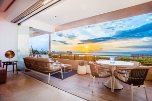 Una sala de estar moderna con un balcón grande que ofrece vistas a un atardecer.