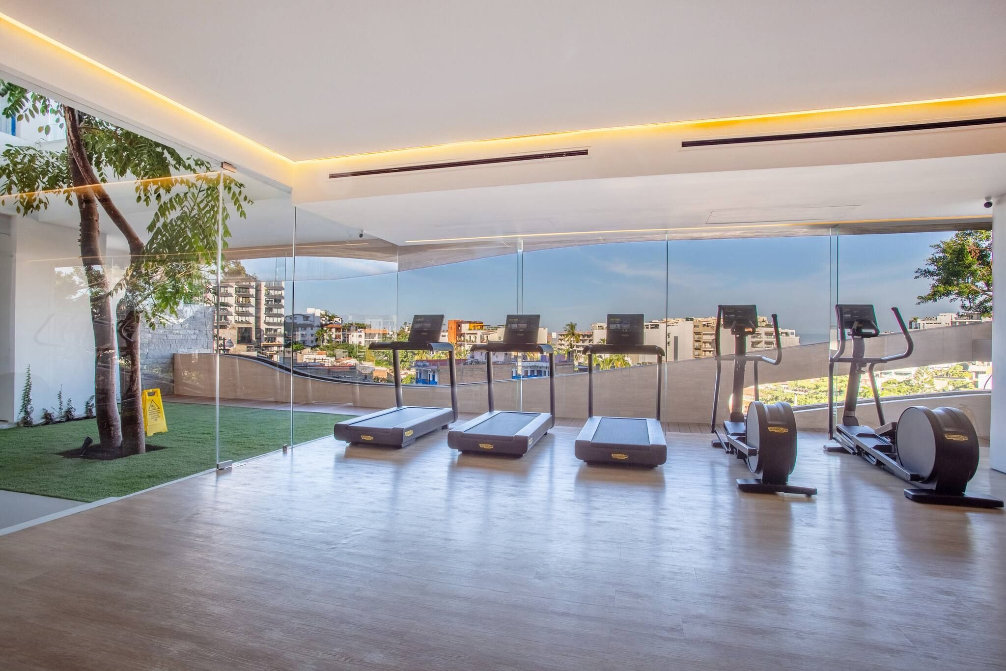 Une salle de sport moderne équipée de tapis de course, d’un rameur et d’un vélo d’appartement, avec de grandes fenêtres offrant une vue sur la ville.