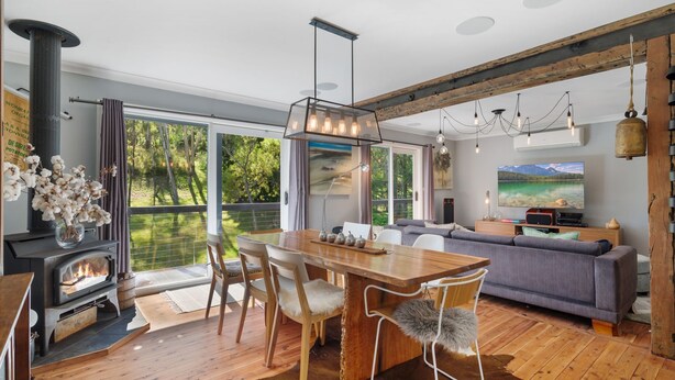 A modern living room with a large wooden dining table, comfortable seating, a fireplace, and a large window offering a view of the outdoors.