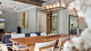 A modern dining area with a wooden table, white chairs, and a chandelier.