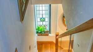 A wooden staircase with glass railings leading to a landing with a window and plants. - The Church Vaults (Matlock)