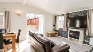 A living room with a sofa, a dining table with chairs, a fireplace, and a TV. - Lake View Lodge (Windermere)