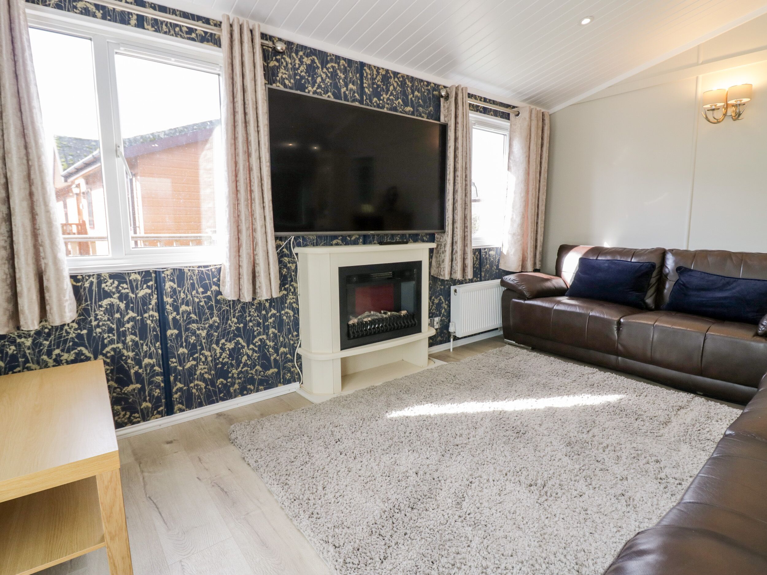 A living room with a fireplace, a brown leather sofa, and a television mounted above it.
