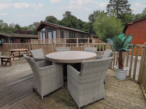 Eine Holzterrasse mit Korbmöbeln, darunter ein runder Tisch und Stühle, sowie ein Blumentopf.