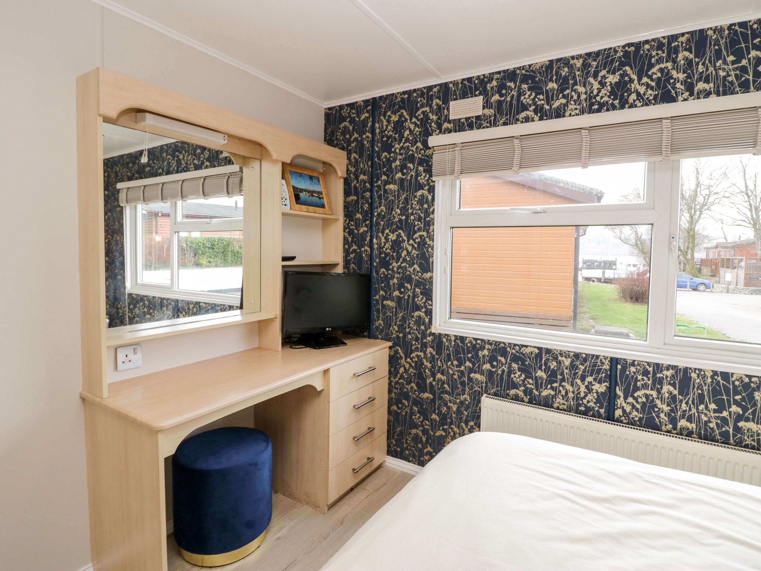 Ein Schlafzimmer mit Holzschreibtisch, Fernseher, Bett und Fenster mit Jalousien.