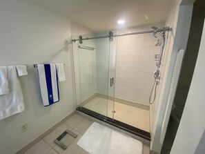 A modern bathroom with a glass-enclosed shower, white tiled walls, and a white floor.