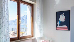 A room with a large window, a view of mountains, a framed artwork on the wall, and a red chair. - Graziella House (Brenzone sul Garda)