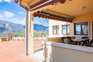 A terrace with a table and chairs, a view of mountains, and a building with windows. - Graziella House (Brenzone sul Garda)