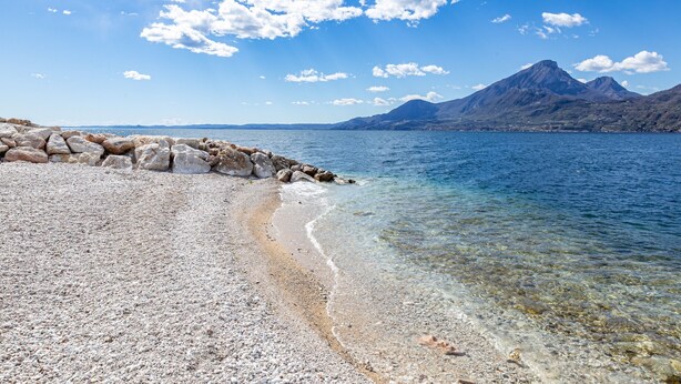 A pebble beach with clear water and a mountain in the background. - Graziella House (Brenzone sul Garda)