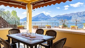 A terrace with a table set for dining, overlooking a lake and mountains. - Graziella House (Brenzone sul Garda)
