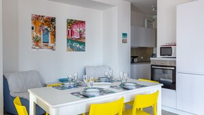 A dining area with a white table set for four, yellow chairs, and two colorful paintings on the wall. - Graziella House (Brenzone sul Garda)