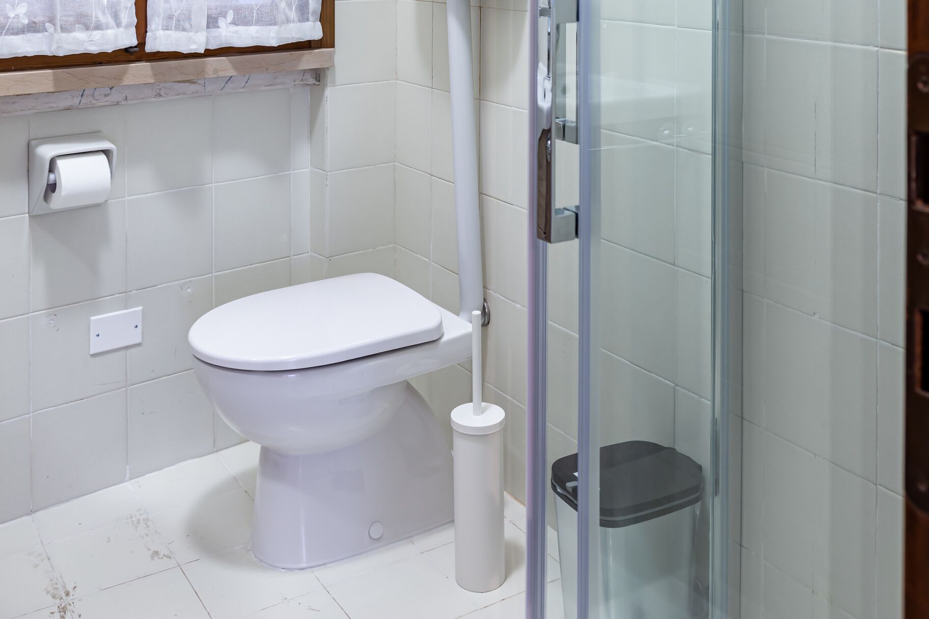 Un bagno con un water, un cestino e un box doccia in vetro.