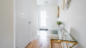 Un couloir avec une porte blanche, une table en verre ornée d’une plante et un miroir décoratif accroché au mur.