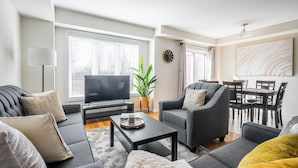 Un salon moderne comprenant un canapé, un fauteuil, une table basse, un téléviseur et un coin repas avec des chaises et une table.
