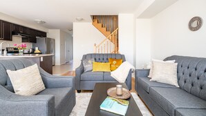 Un salon moderne avec des canapés gris, une table basse sur laquelle repose un livre et un escalier menant à l’étage supérieur.