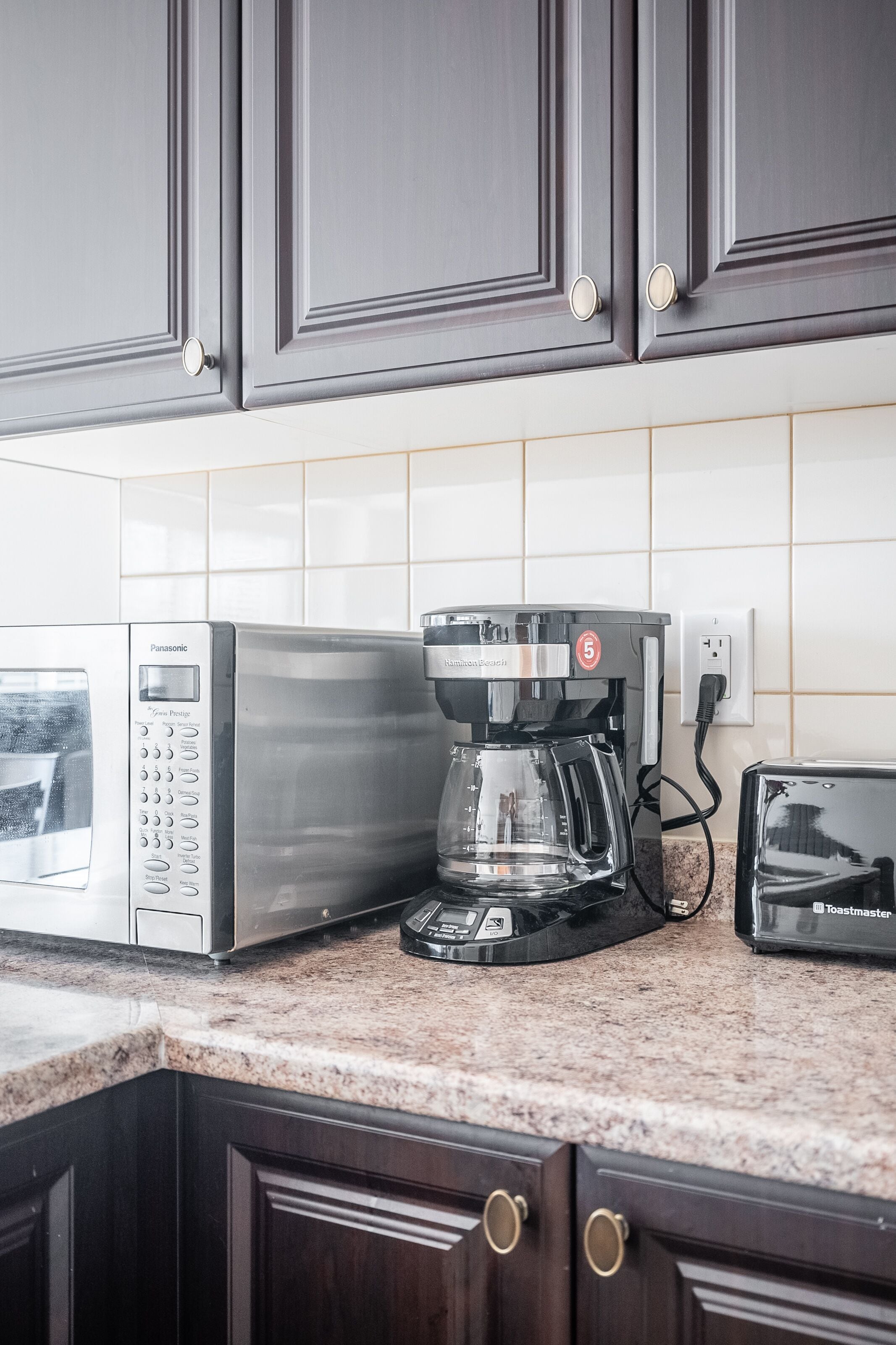 A kitchen with dark wooden cabinets, a microwave, a coffee maker, and a toaster.