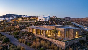 Un edificio moderno de piedra con techo plano, ventanas amplias y un camino pavimentado que conduce hacia él.
