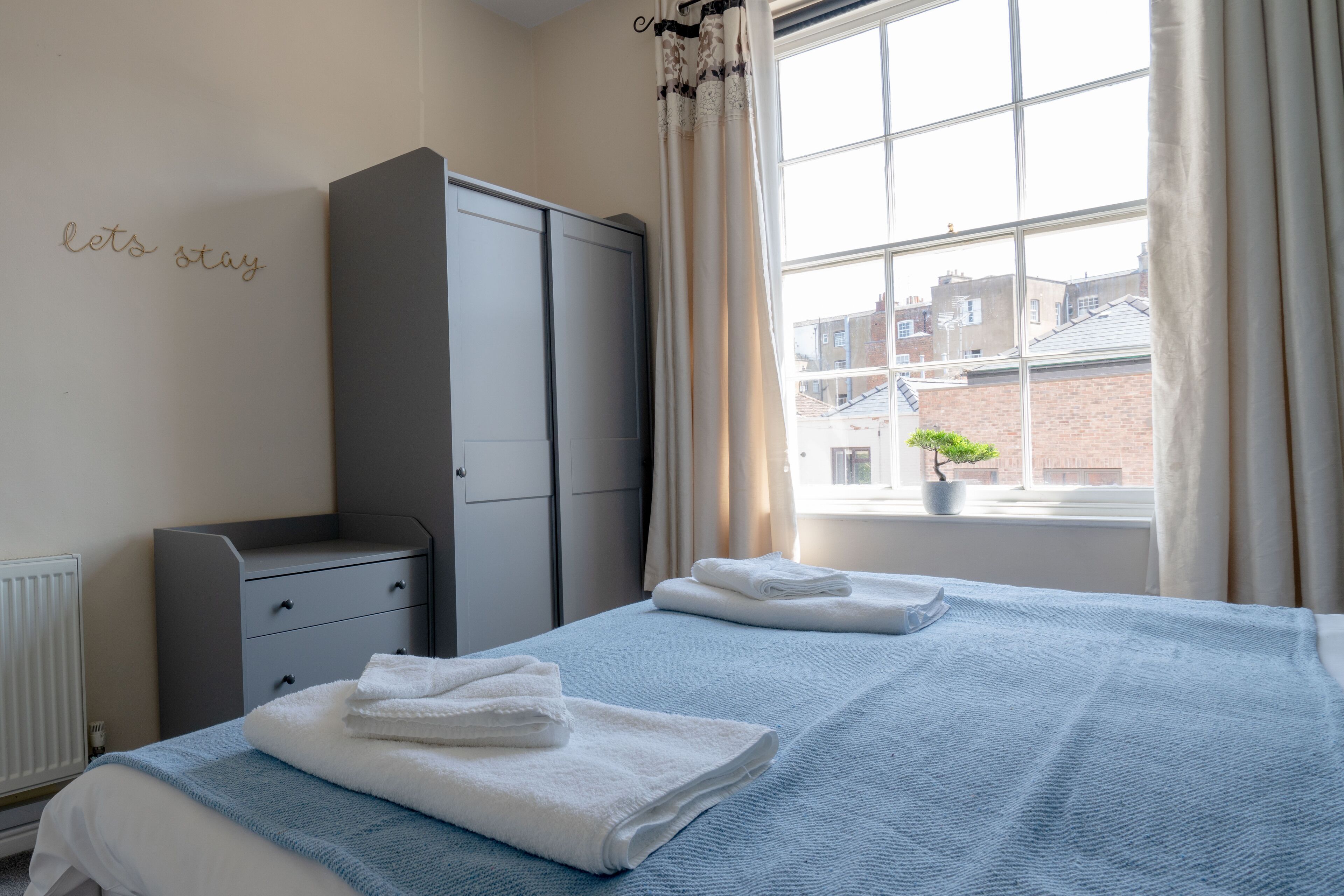 A bedroom with two beds, a grey wardrobe, a window with curtains, and a radiator.