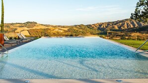 Una piscina rectangular con agua cristalina azul, rodeada de sillas de descanso y vistas a un terreno montañoso.