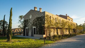 Un edificio de piedra con un ventanal grande y una puerta, rodeado de follaje y un camino de grava.