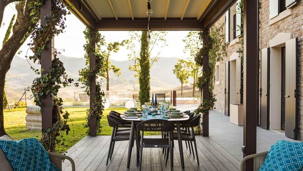 Un patio al aire libre con una mesa de comedor dispuesta para seis personas, rodeada de sillas, y vistas al campo.