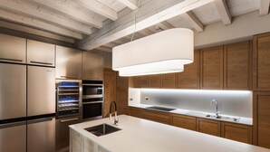 Une cuisine moderne dotée d’appareils électroménagers en acier inoxydable, d’un îlot central avec un évier, de meubles en bois et de poutres apparentes au plafond.