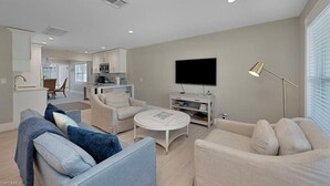 Una sala de estar moderna con un sofá, un sillón y una mesa de centro. Hay un televisor de pantalla plana montado en la pared y una lámpara de pie.
