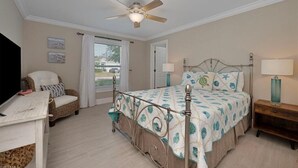 Un dormitorio con cama, ventilador de techo, una silla, lámpara y televisor.