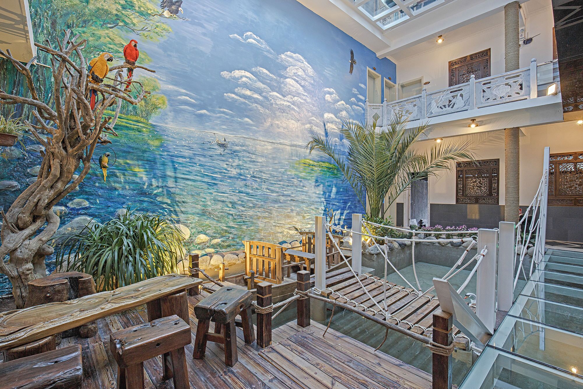 Un espacio interior amplio con un mural de paisaje tropical, mobiliario de madera y una escalera de cristal.