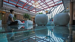 A modern interior with a glass ceiling, a person sitting on a sofa, and a large bird sculpture. - China Old Story Inns Dali Elite Garden (Dali)