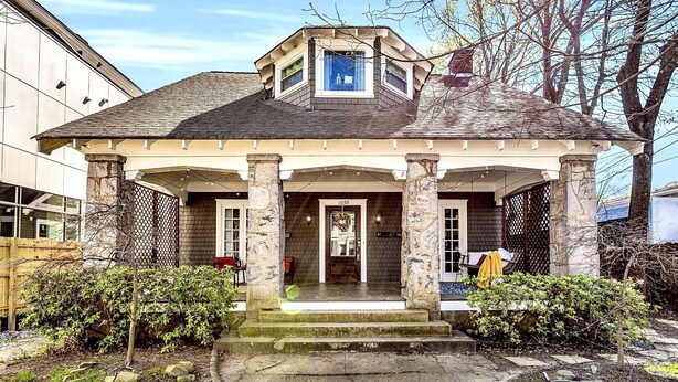A two-story house with a covered porch, stone columns, and a small attic window. - 1929 Historic Craftsman Bungalow | King Bed (Atlanta)
