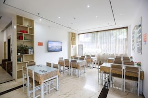 A room with multiple tables and chairs, a television, and shelves with various items. - Jinxiu Holiday Hotel (Yangshuo)