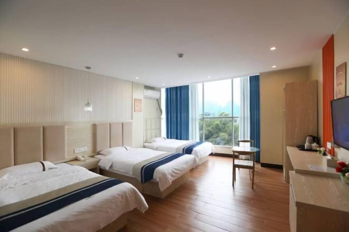 A hotel room with two beds, a small table, a TV, and a window with curtains.