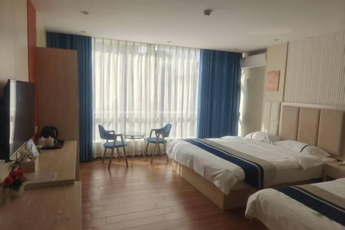 A hotel room with two beds, a desk with a chair, a TV, and a window with curtains.